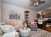 Thumbnail 21 of 27 - A living room with a beige couch, a grey armchair, a white coffee table, and a painting of a city skyline on the wall.