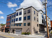 Thumbnail 9 of 14 - A modern building with a grey facade and a red brick building in the background.
