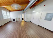 Thumbnail 8 of 12 - A spacious room with wooden floors and white walls.