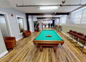 Thumbnail 4 of 12 - A pool table in a room with wooden flooring and chairs.