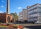 Thumbnail 12 of 12 - A brick building with a tall chimney is in front of a modern building.