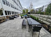 Thumbnail 16 of 53 - A patio with a table and chairs is in front of a building.