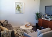 Thumbnail 3 of 12 - A living room with a brown couch, a white ottoman, and a painting on the wall.