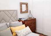 Thumbnail 11 of 12 - A bed with a grey headboard and pillows in front of a mirror and a dresser.