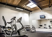 Thumbnail 8 of 12 - A gym with a wooden ceiling and a television mounted on the wall.