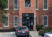 Thumbnail 2 of 12 - A black car is parked in front of a brick building with the number 33 on the door.