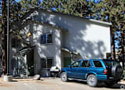 Thumbnail 9 of 18 - A blue car is parked in front of a white house.