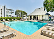 Thumbnail 11 of 19 - A large swimming pool surrounded by sun loungers and a building in the background.