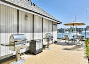 Thumbnail 15 of 19 - A patio with a grill and chairs overlooking a body of water.
