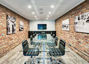 Thumbnail 21 of 24 - A conference room with a glass table and chairs, a television, and framed pictures on the brick walls at The Meadows Apartments, Culver City , CA 90230