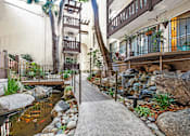Thumbnail 2 of 10 - A small pond with rocks and a wooden walkway in the middle of a courtyard.