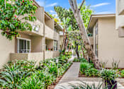 Thumbnail 17 of 18 - A row of beige apartment buildings with green plants in front at West Park Village, Los Angeles, CA