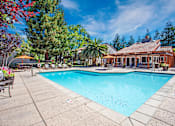 Thumbnail 1 of 17 - A large swimming pool surrounded by trees and a house in the background at Valley Plaza Villages, California, 94566