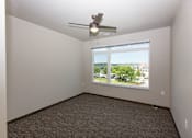Thumbnail 18 of 19 - A room with a ceiling fan and a window overlooking a parking lot.