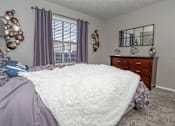 Thumbnail 11 of 37 - Ambassador bedroom with a large bed and a wooden dresser at The Oasis apartments in Bossier City, LA