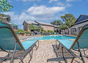 Thumbnail 10 of 23 - Blue lounge chairs by the pool with apartments in the background at The Pearl apartments in Shreveport, LA