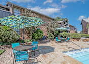 Thumbnail 11 of 23 - Poolside seating with shaded tables and chairs at The Pearl apartments in Shreveport, LA