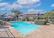 Thumbnail 9 of 23 - A swimming pool surrounded by a stone border and a residential area.