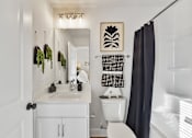 Thumbnail 9 of 13 - A white bathroom with a toilet, sink, and a mirror.