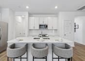 Thumbnail 4 of 49 - A modern kitchen with a white island and grey chairs.