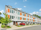 Thumbnail 1 of 16 - A red car is parked in front of a building with orange and grey panels.