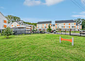 Thumbnail 15 of 16 - A grassy area in front of apartment buildings with a fence and orange barrier.