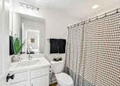 Thumbnail 13 of 16 - A bathroom with a white sink, toilet, and a shower curtain.