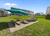Thumbnail 25 of 29 - A picnic area with a green canopy and benches is set in a grassy area.