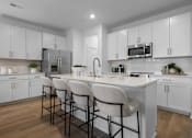 Thumbnail 25 of 49 - A kitchen with white cabinets and a white island with three chairs.