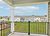 Thumbnail 12 of 16 - A balcony with a black railing overlooks a grassy area and buildings.