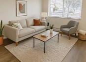 Thumbnail 6 of 11 - A living room with a grey sofa, a grey armchair, a wooden coffee table, and a large window with blinds.