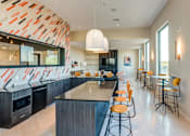 Thumbnail 11 of 23 - A modern kitchen with a bar area and orange chairs.