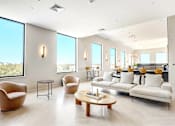 Thumbnail 10 of 23 - A living room with a white sofa, a coffee table, and a large window with a view of the city.
