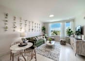Thumbnail 2 of 23 - A living room with a green couch, a white table, and a TV on the wall.
