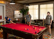 Thumbnail 28 of 48 - Three People Playing in Game Room With Pool Table at Midtown Sam Houston Apartments, Huntsville, 77340