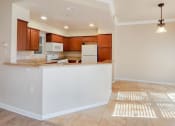 Thumbnail 18 of 54 - View from living area into kitchen and dining area. Brown cabinets, white appliances, tile flooring and wood look flooring, recessed lighting, wrap around kitchen counter.