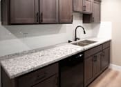 Thumbnail 10 of 19 - A kitchen with a granite countertop and dark brown cabinets.
