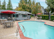 Thumbnail 7 of 19 - A pool with a red umbrella and a house in the background at Sierra Oaks Living Apartments, Cameron Park, CA