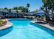 Thumbnail 34 of 46 - A large swimming pool with a blue tinted water surrounded by a fence and trees.