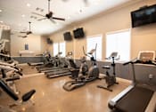 Thumbnail 18 of 61 - A spacious gym with treadmills, elliptical machines, and a television.