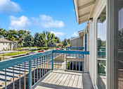 Thumbnail 3 of 24 - A balcony with a blue railing overlooks a parking lot and trees.