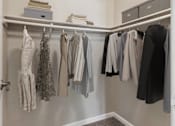 Thumbnail 8 of 24 - A closet with clothes hanging on a rail and a shelf above.