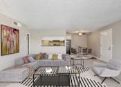 Thumbnail 9 of 24 - A living room with a grey couch, a glass coffee table, and a painting on the wall.