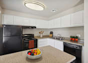 Thumbnail 11 of 24 - A kitchen with a black refrigerator, white cabinets, and a bowl of fruit on the counter.