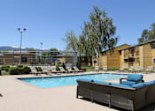 Thumbnail 19 of 24 - A pool with a couch and chairs in the foreground and a building in the background.