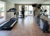 Thumbnail 32 of 33 - a gym with cardio equipment and windows in a building with wood floors
