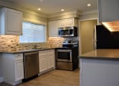 Thumbnail 15 of 16 - View of kitchen featuring stainless appliances, white cabinets, tile back splash, window above the sink and wood like flooring.