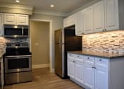 Thumbnail 14 of 16 - View of kitchen featuring stainless appliances, white cabinets, tile back splash and wood like flooring.
