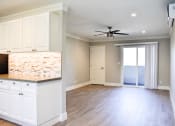 Thumbnail 5 of 16 - View of living area with wood-like flooring, ceiling fan, entrance to patio, and partial view of kitchen counter and cabinet at Americana La Crescenta