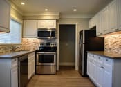 Thumbnail 6 of 16 - View of the kitchen, featuring wood like floors, stainless appliances, tile backsplash, white cabinets, window view over sink with wood-like blinds